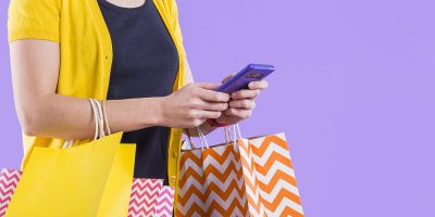 close-up-woman-s-hand-using-cellphone-white-carrying-shopping-bag